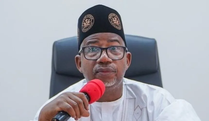 Portrait of an official speaking into a microphone, used as the source image for the education scorecard report.