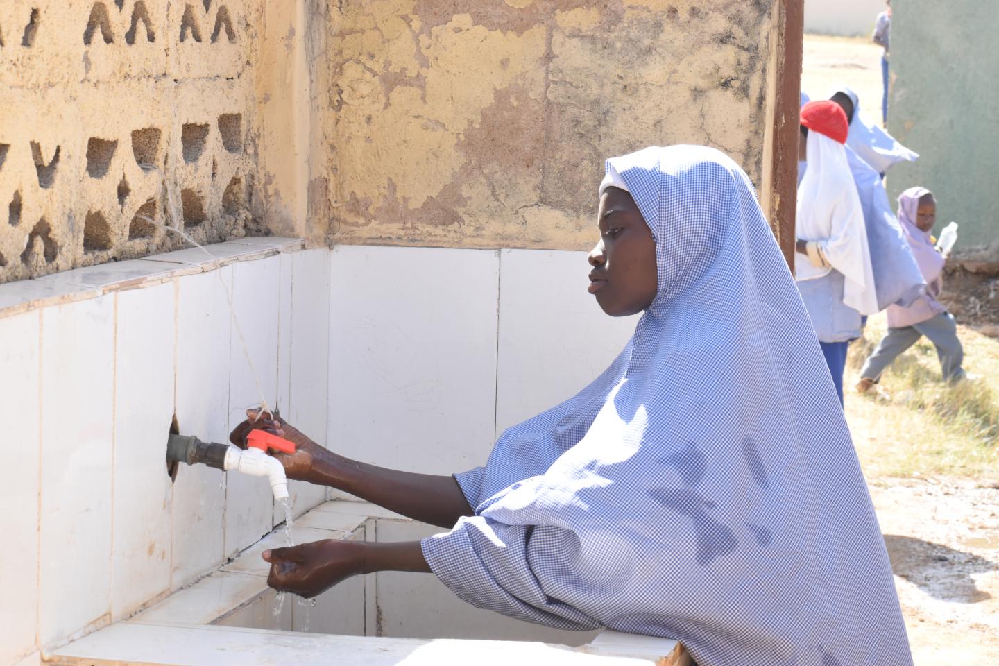 A person using a community hand-pump water point, used as a UNICEF WASH source image.